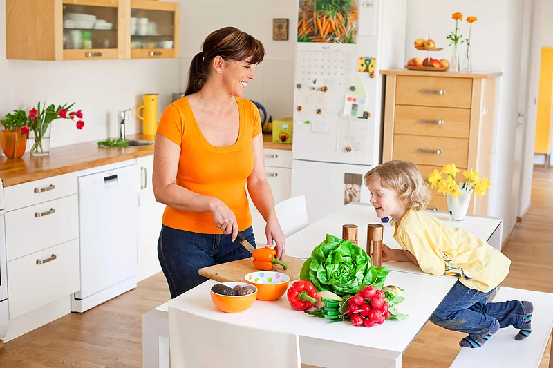 Haushaltshilfe, die das Essen vorbereitet, und Kind sitzt daneben