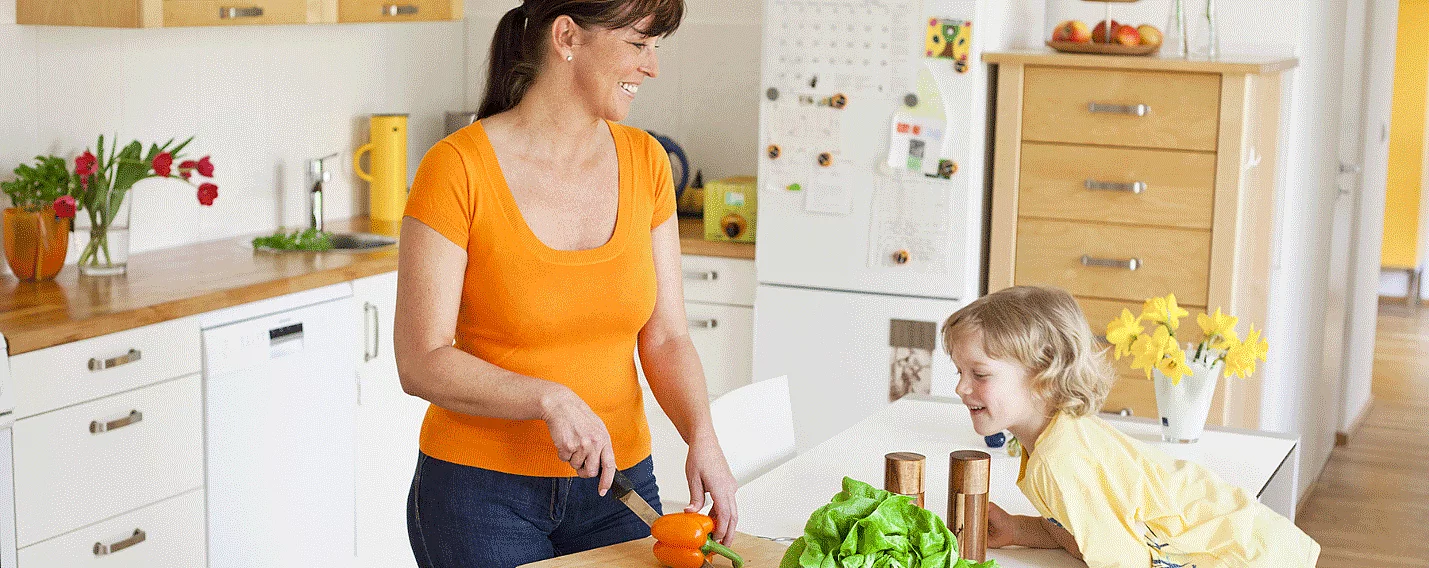 Haushaltshilfe, die das Essen vorbereitet, und Kind sitzt daneben